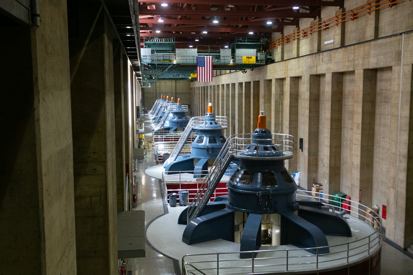 American flag hangs above large industrial turbine generators in a facility.