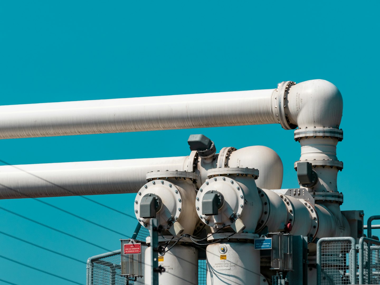 Industrial high-voltage equipment with white pipes against blue sky.