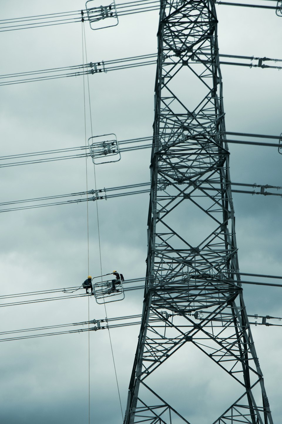 Technicians working on high-voltage power lines against a cloudy sky.